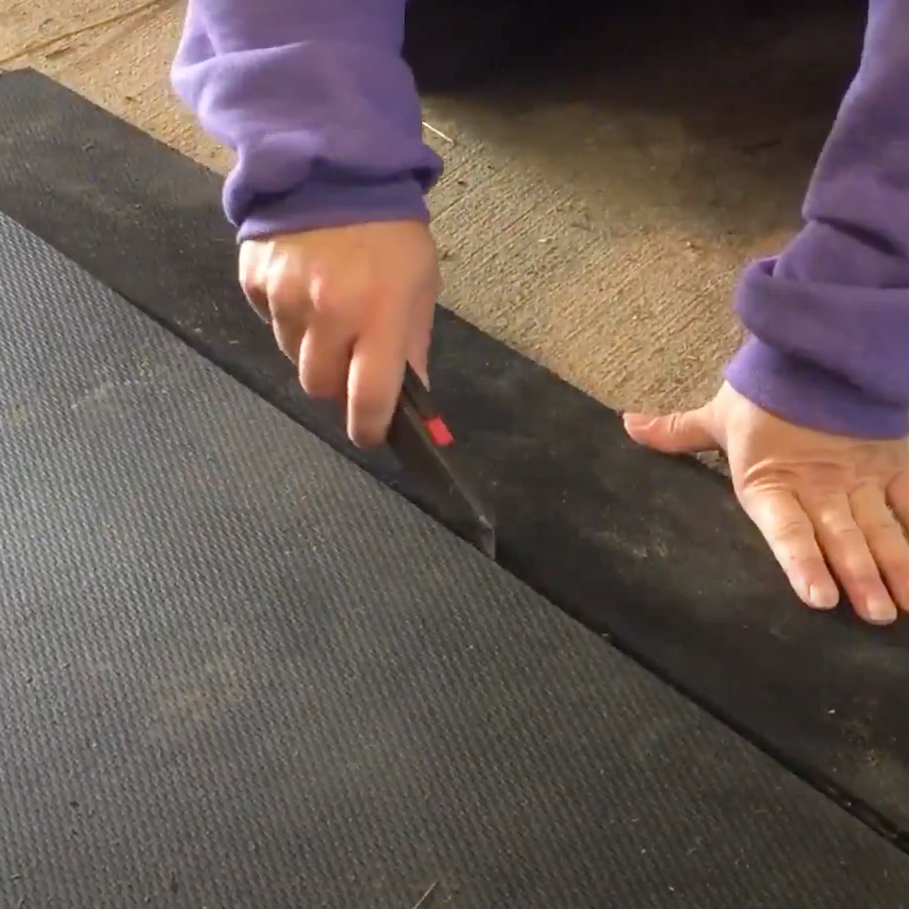 person cutting large rubber horse stall mats with utility knife