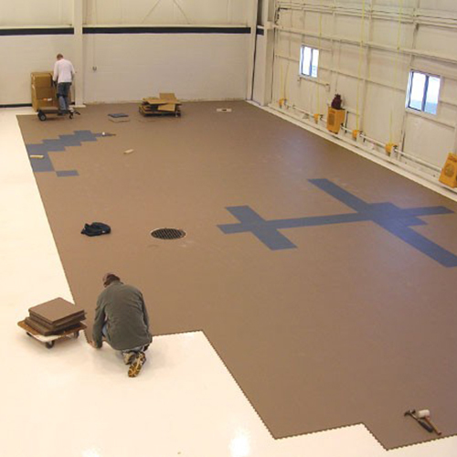 two people installing gray and tan tiles in airplane hangar