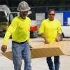 Two workers carrying Blue Gator Ground Protection Diamond Mat 1/2 Inch x 4x8 Ft. in tan