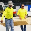 Two guys carrying Blue Gator Lite Ground Protection Diamond Mat Tan 3/8 Inch x 4x8 Ft.